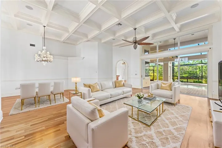 Living room with a high ceiling, coffered ceiling, ceiling fan with notable chandelier, light hardwood / wood-style flooring, and beamed ceiling