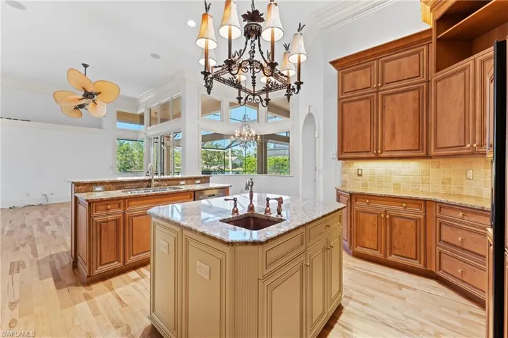 Kitchen featuring light stone counters, ornamental molding, ceiling fan with notable chandelier, a kitchen island with sink, and pendant lighting