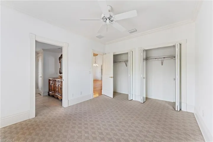 Unfurnished bedroom with ceiling fan, crown molding, light carpet, and two closets