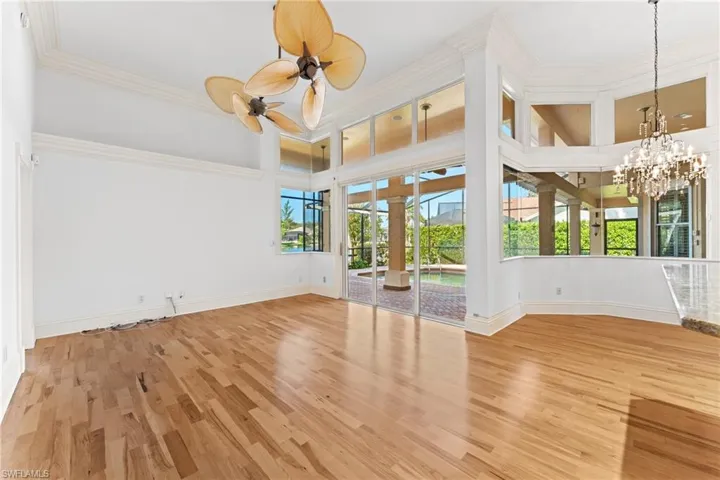 Spare room with hardwood / wood-style flooring, ceiling fan with notable chandelier, crown molding, and a high ceiling