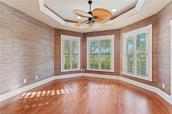 Unfurnished room with ceiling fan, a raised ceiling, ornamental molding, and wood-type flooring