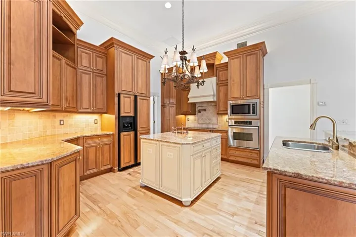 Kitchen with sink, hanging light fixtures, light stone counters, a center island with sink, and appliances with stainless steel finishes