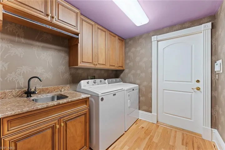 Laundry area with washer and dryer, light wood-type flooring, cabinets, and sink