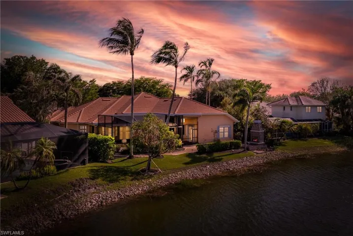 Back house at sunset featuring a lawn, glass enclosure, and a water view