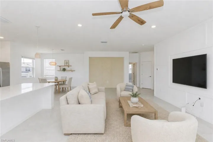 Open-concept living area featuring a wood-finish ceiling fan, recessed lighting, a built-in media wall, a kitchen island with a light-toned countertop, and pendant lighting