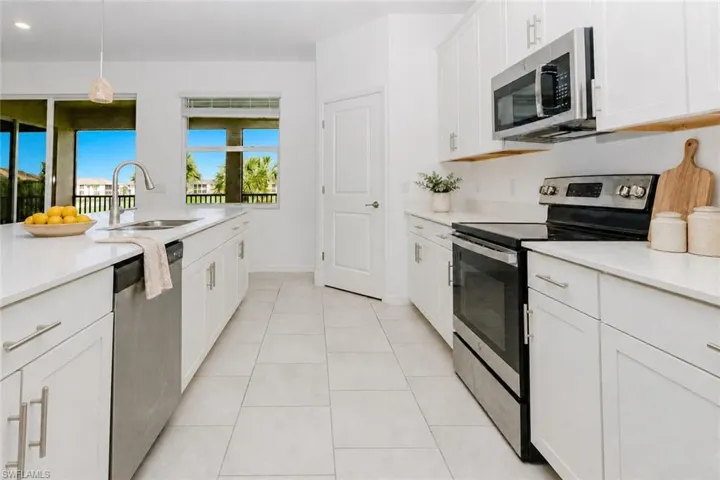 Kitchen featuring white cabinetry, light-toned countertops, stainless steel appliances, and large format floor tiling