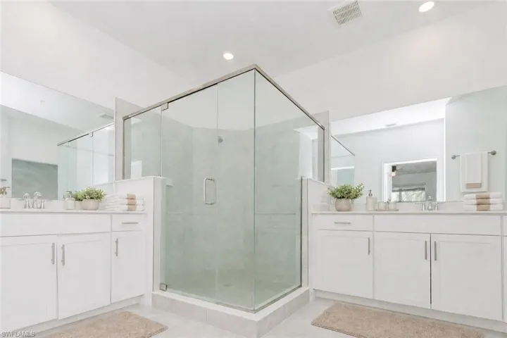 Dual vanities with white cabinetry, a glass-enclosed shower, polished chrome fixtures, and recessed lighting