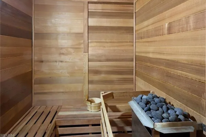 Wood-paneled sauna featuring tiered wooden benches and a stone-filled heater