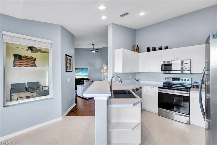 Kitchen with stainless steel appliances, sink, kitchen peninsula, light tile patterned flooring, and ceiling fan