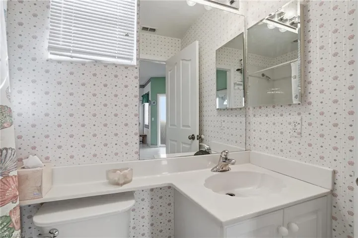Bathroom with wallpapered walls, a shower, and vanity