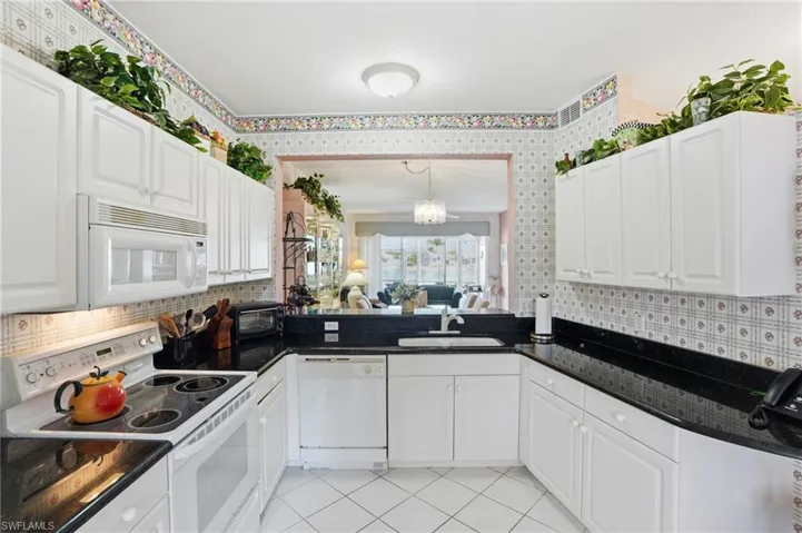 Kitchen with white appliances, white cabinetry, a chandelier, light tile patterned floors, and dark stone counters
