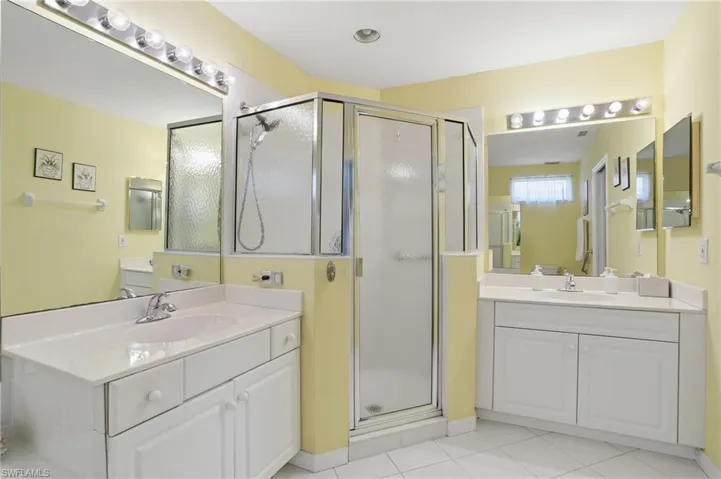 Full bathroom featuring a shower stall, two vanities, and light tile patterned floors