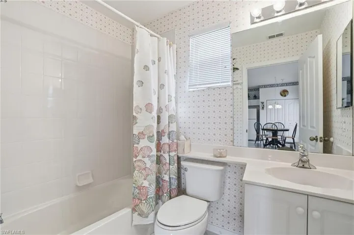 Bathroom with shower / tub combo with curtain, vanity, and wallpapered walls