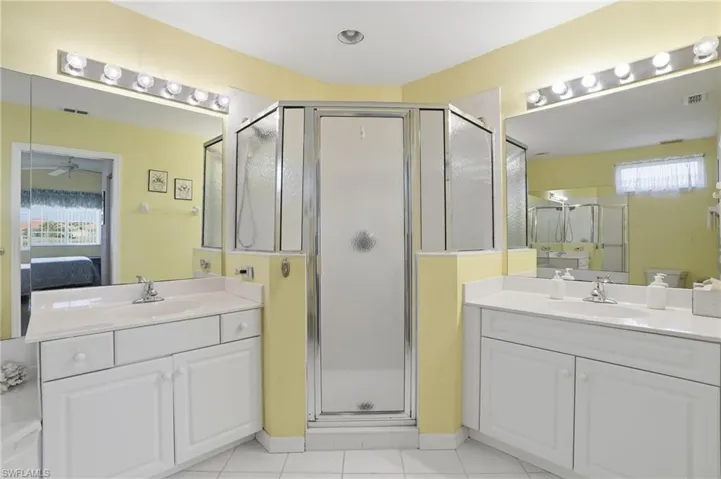 Ensuite bathroom featuring two vanities, a shower stall, and light tile patterned floors