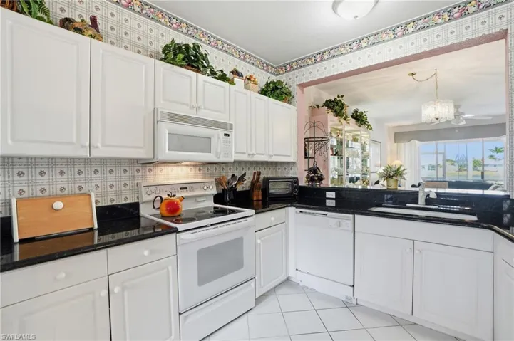 Kitchen featuring white appliances, white cabinets, dark stone counters, light tile patterned floors, and suspended lighting