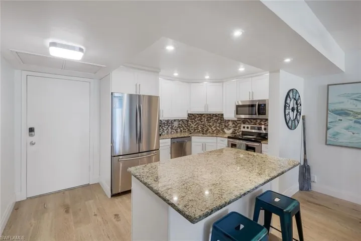 Kitchen featuring white shaker cabinetry, stainless steel appliances, a mosaic tile backsplash, and a breakfast bar with granite countertops