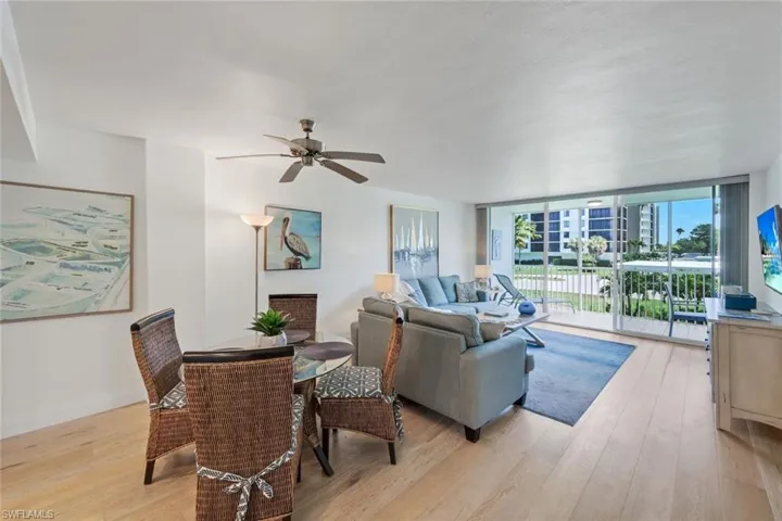 Open-concept living space featuring light wood-finish flooring, a contemporary ceiling fan, and abundant natural light from the large sliding glass doors