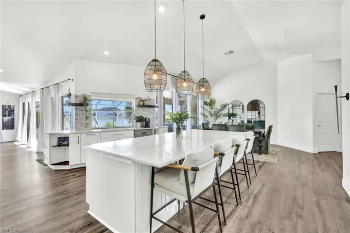 Kitchen with white cabinets, a kitchen breakfast bar, lofted ceiling, decorative light fixtures, and light wood finished floors