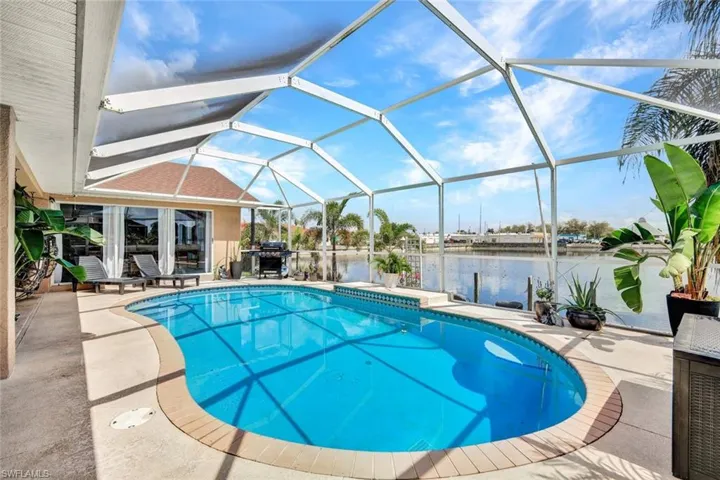 Swimming pool featuring a sunroom, glass enclosure, a patio area, a water view, and grilling area