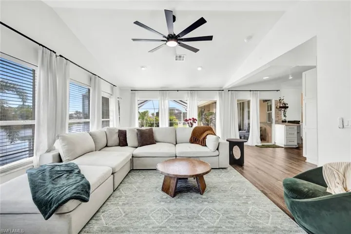 Living room with lofted ceiling, a ceiling fan, and light wood-style flooring