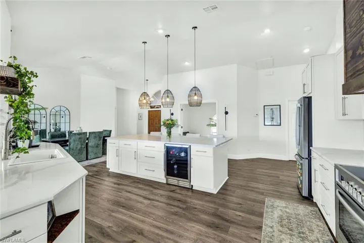 Kitchen with white cabinets, beverage cooler, stainless steel appliances, a center island, and dark wood-style floors