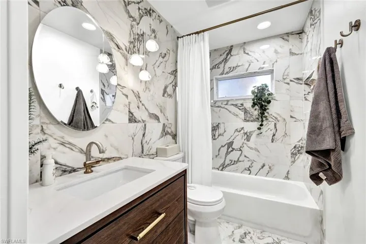 Bathroom with vanity, light marble finish flooring, tile walls, shower / tub combo, and recessed lighting