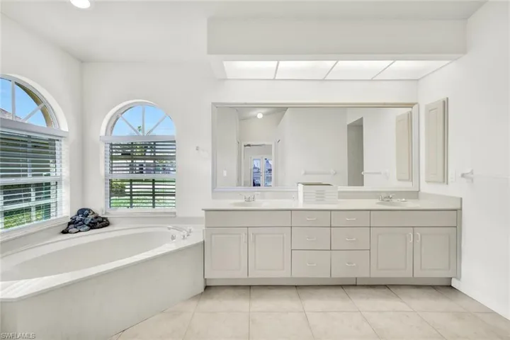 Bathroom with double vanity, light tile patterned floors, and a garden tub