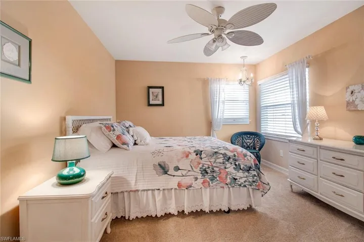 Bedroom featuring light colored carpet and ceiling fan with notable chandelier
