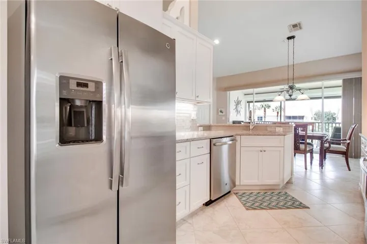 Kitchen with stainless steel appliances, light stone countertops, white cabinetry, and tasteful backsplash