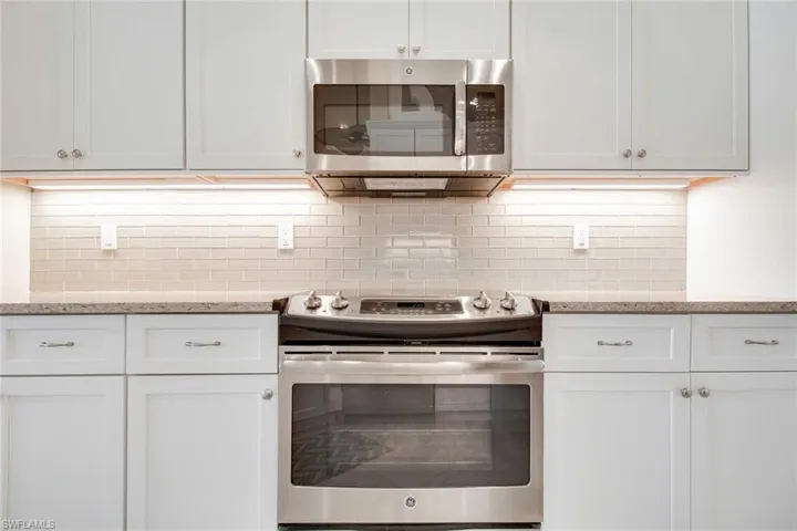 Kitchen featuring white cabinets, decorative backsplash, appliances with stainless steel finishes, and light stone counters