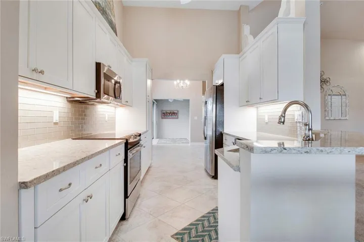 Kitchen with white cabinets, sink, light tile patterned flooring, light stone countertops, and appliances with stainless steel finishes