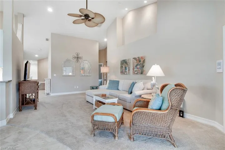 Living room with light colored carpet, ceiling fan, and a high ceiling
