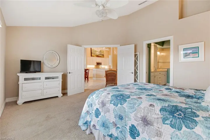 Bedroom featuring ceiling fan, ensuite bath, light carpet, and high vaulted ceiling