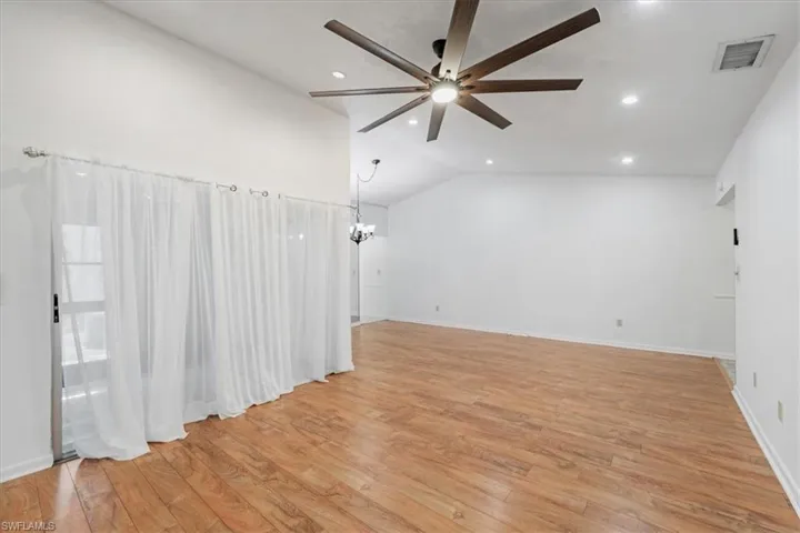 Unfurnished room featuring ceiling fan with notable chandelier, vaulted ceiling, and light hardwood / wood-style flooring