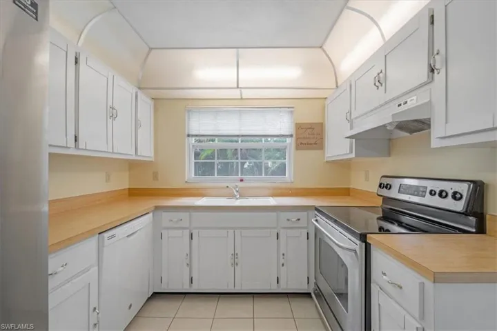 Kitchen featuring sink, white cabinets, light tile flooring, and appliances with stainless steel finishes