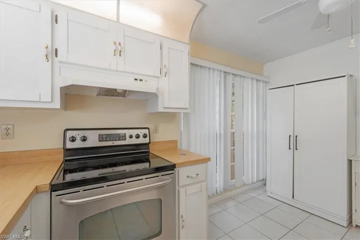 Kitchen featuring stainless steel range with electric stovetop, ceiling fan, custom exhaust hood, white cabinetry, and light tile floors