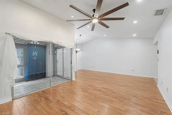 Spare room with vaulted ceiling, light hardwood / wood-style flooring, and ceiling fan with notable chandelier