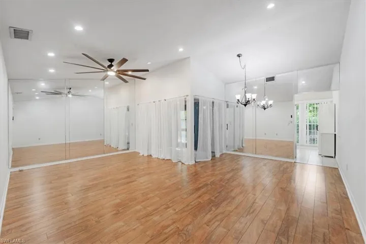 Unfurnished room featuring high vaulted ceiling, light wood-type flooring, and ceiling fan with notable chandelier