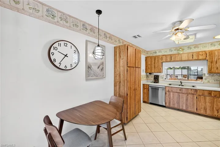 Kitchen featuring hanging light fixtures, light countertops, light tile patterned floors, brown cabinets, and dishwasher