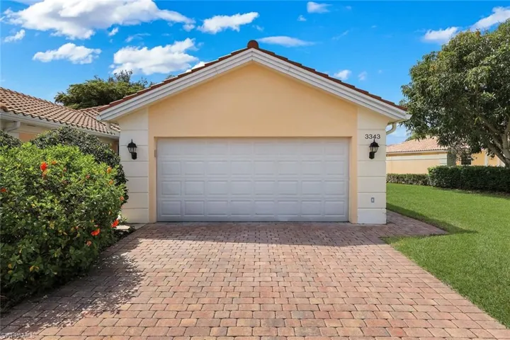Front exterior featuring a two-car garage with paneling, a concrete tile roof, and a paver driveway