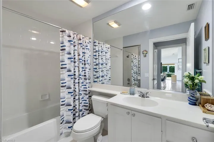 Full bathroom featuring a white vanity with integrated sink, a large wall-mounted mirror, white paneled cabinetry, and a combination shower and bathtub with white subway tile surround