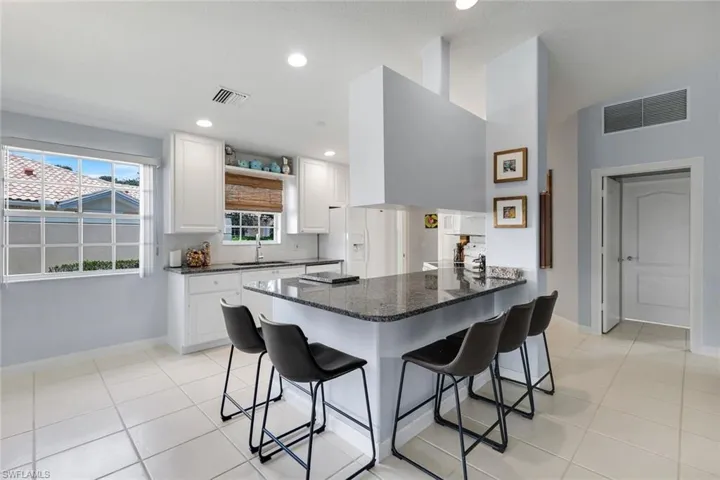 Kitchen featuring white shaker cabinetry, speckled stone countertops, tile flooring, recessed lighting, and a window with horizontal muntins