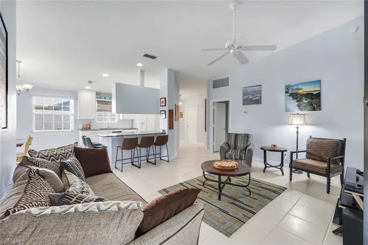 Open-concept living space featuring light-colored tile flooring, vaulted ceilings, and a ceiling fan