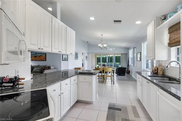 Spacious kitchen featuring white cabinetry, dark granite countertops, a built-in cooktop, and a double basin stainless steel sink