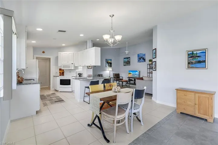 Open-concept living space featuring a white kitchen, light-colored tile flooring, granite countertops, recessed lighting, and a dining area with a chandelier