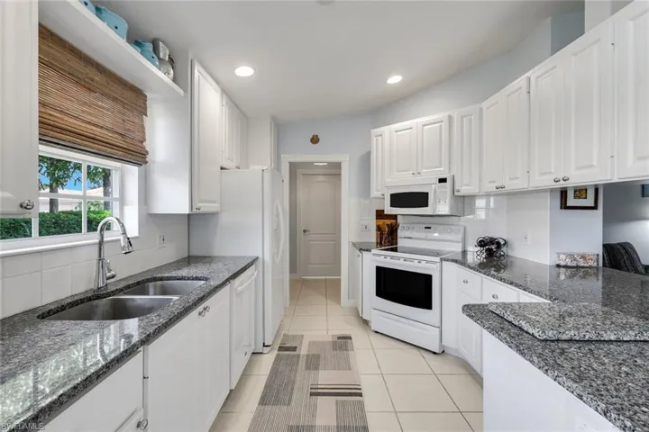 Galley kitchen featuring white cabinetry, stone countertops, white tile backsplash, and a double basin stainless steel sink