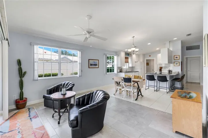 Spacious open-concept living area featuring light gray tile flooring, white ceiling fan, and two large windows