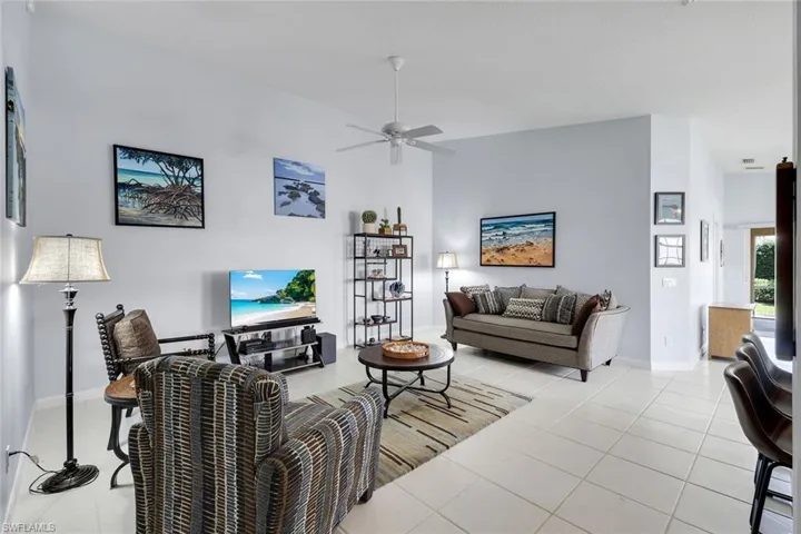 Spacious living area featuring light-toned tile flooring, vaulted ceilings, and a ceiling fan