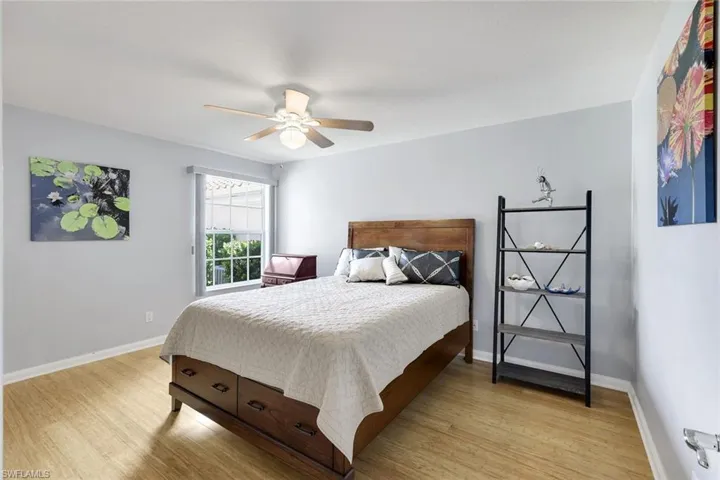 Spacious room featuring wood-finish flooring, light gray walls, a window with exterior green foliage, and a ceiling fan with integrated lighting