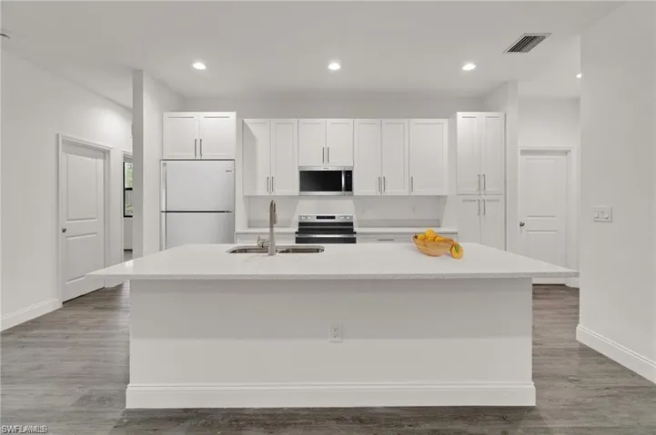 Kitchen with range, white cabinetry, white fridge, hardwood / wood-style floors, and a center island with sink